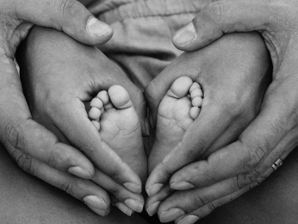 Familienaufstellung: Babyfüße werden von Mutterhänden umschlossen, die wiederum von Vaterhänden gehalten werden