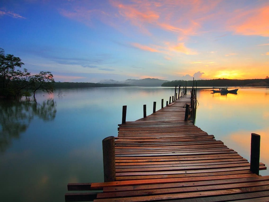 Quantencoaching: Ein Steg führt hinaus auf einen See, der in Sonnenaufgangsstimmung ruhig da liegt